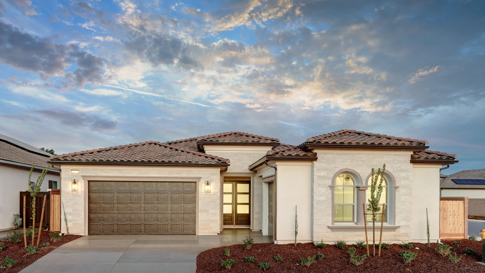 Photo of a Granville Cali home with light stucco, white brick accents, and three garage spaces