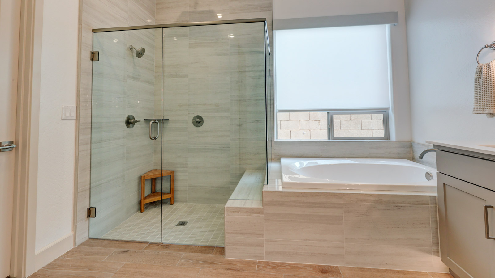 Spacious bath with multi-head shower, stylish tub, and long spacious vanity.
