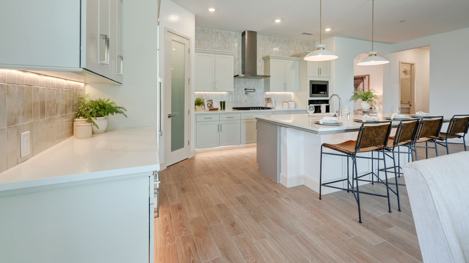 Kitchen with walk-in pantry, island with breakfast bar, stovetop pot filler and plank tile flooring.